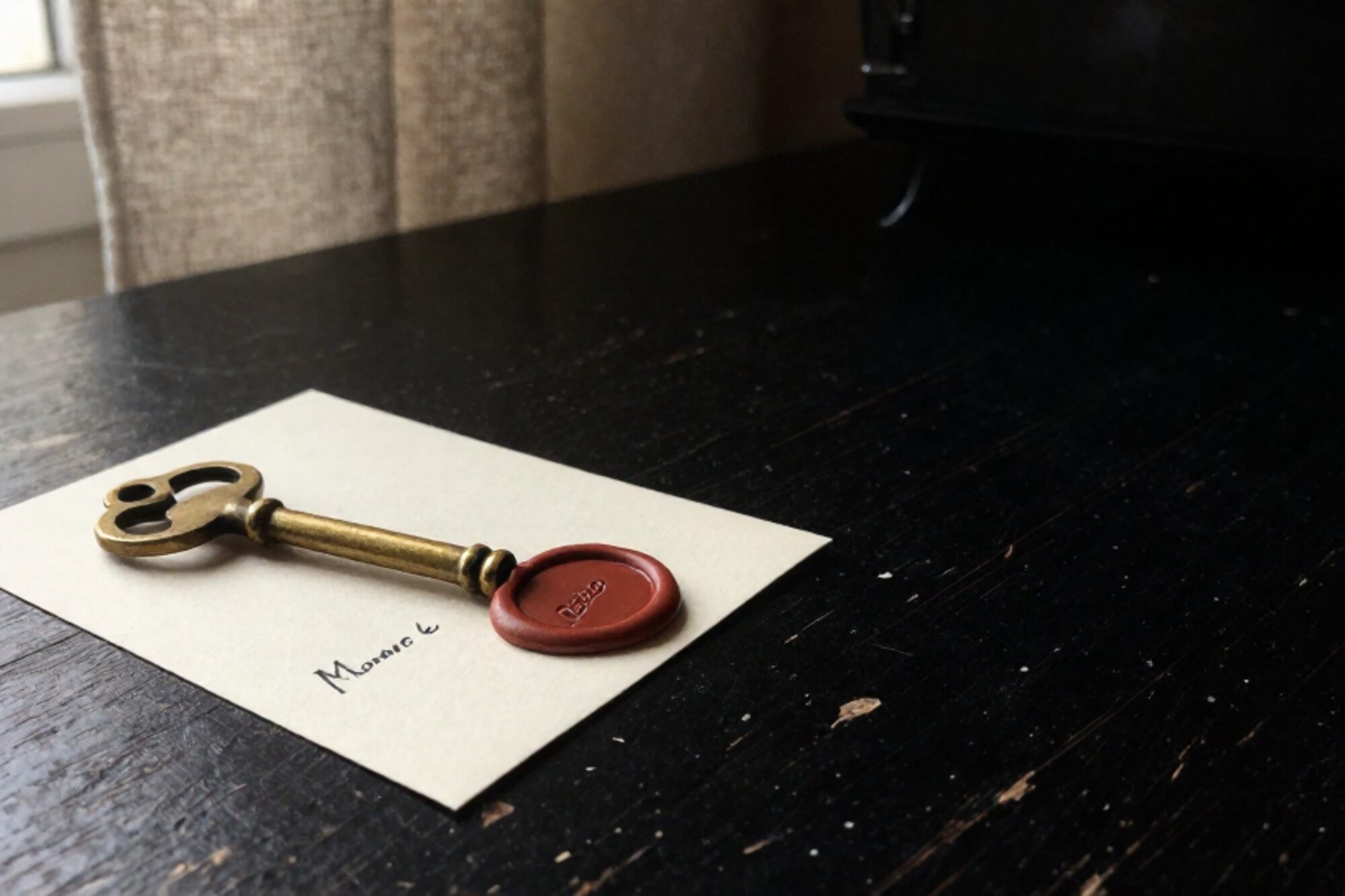 Brass skeleton key on a cream paper card with black stamped label and red wax seal, on scarred dark oak desk.