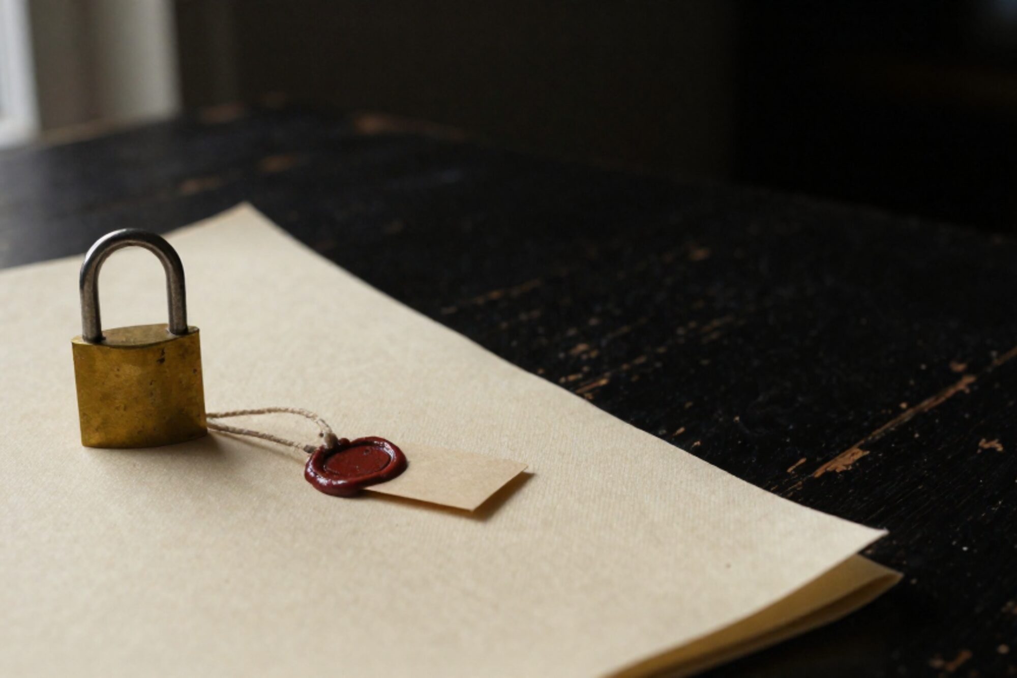 Brass padlock with wax-sealed paper tag on folded linen cloth, bone paper surface, dark oak table edge.
